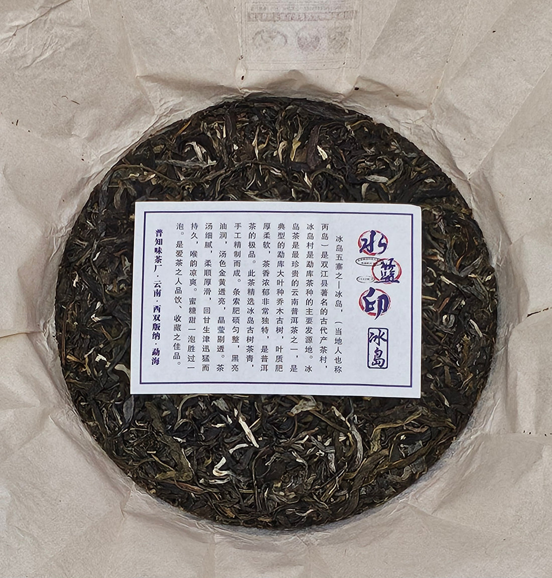 Image 1: A round cake of compressed tea leaves wrapped in paper. The center features a rectangular label with text in Chinese characters, indicating its origin from Bingdao Old Village.